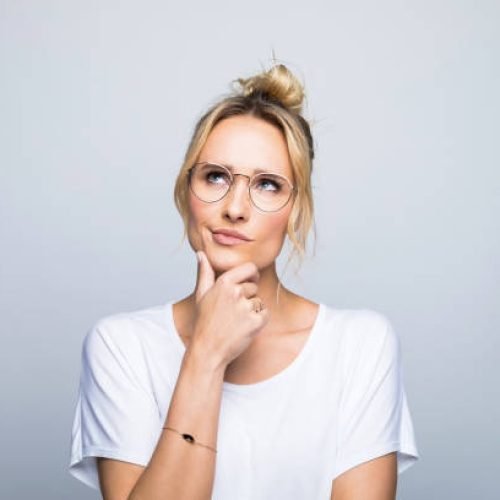 Thoughtful blond woman with hand on chin looking up against gray background